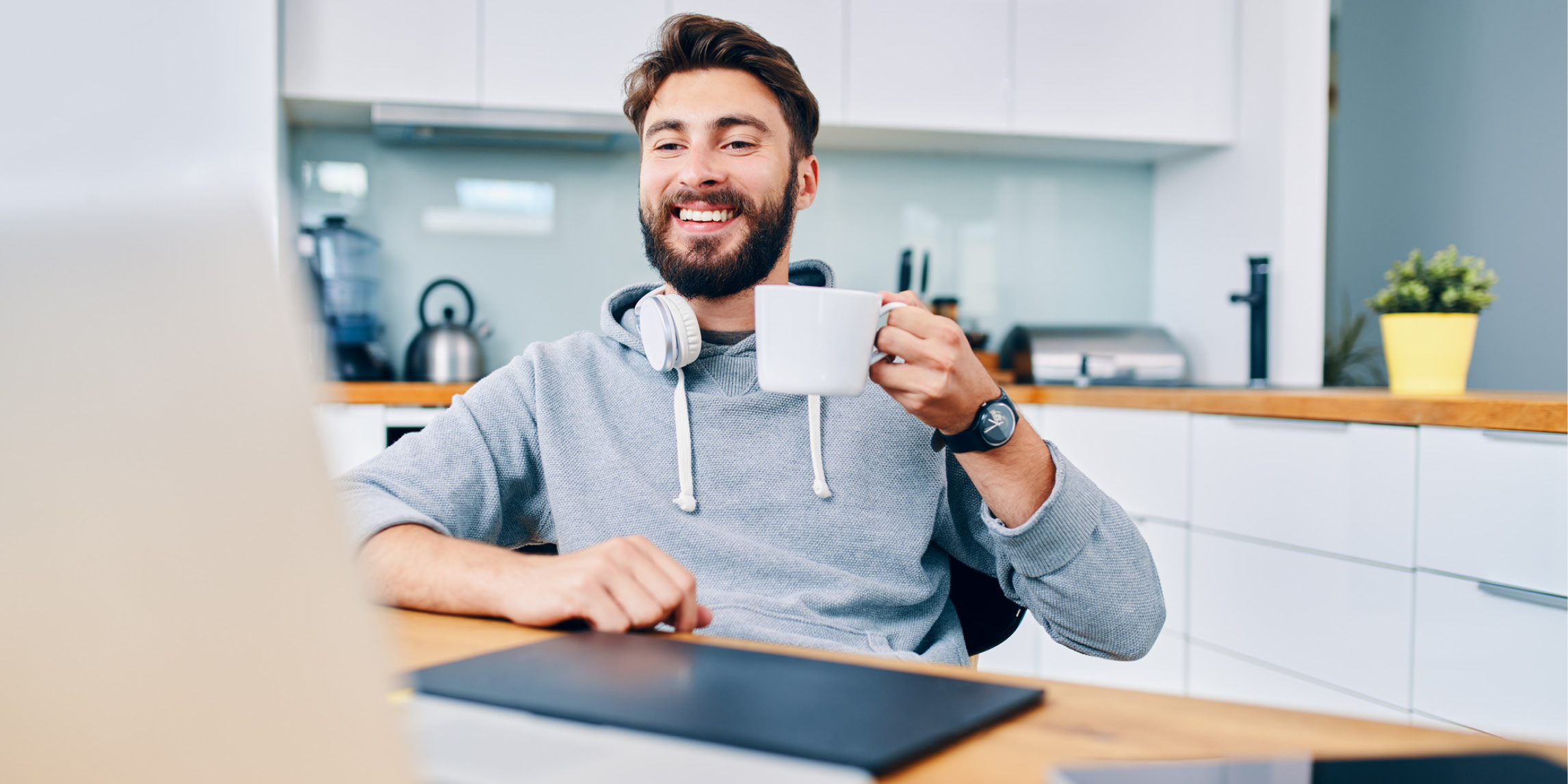 A man smiling and holding a cup in front of a computer