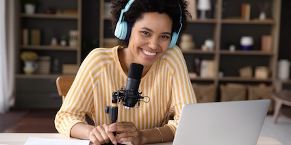 Happy young Black woman in headphones and professional microphone recording